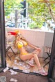 A woman in a yellow bikini sitting on a window sill.