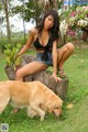 A woman sitting on top of a tree stump next to a dog.