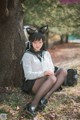 A woman in a school uniform sitting under a tree.