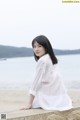 A woman in a white dress sitting on a rock by the water.