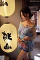 A woman in a blue kimono standing next to a lamp.