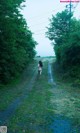 A naked woman walking down a dirt road in the middle of a forest.