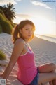 A woman in a pink tank top sitting on a sandy beach.