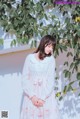 A woman standing in front of a white wall wearing a white dress.