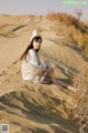 A woman sitting on top of a sand dune in the desert.