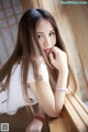 A woman with long brown hair leaning against a wooden wall.