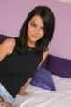 A woman sitting on top of a bed next to a purple pillow.