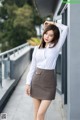 A woman in a white shirt and brown skirt leaning against a wall.