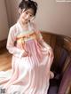 A woman in a pink hanbok sitting on a purple chair.