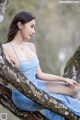 A woman in a blue dress sitting on a tree branch.