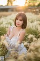 A woman in a white dress sitting in a field of tall grass.