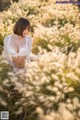 A woman in a white lingerie sitting in tall grass.