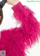 A woman wearing a pink sweater with black feathers on it.